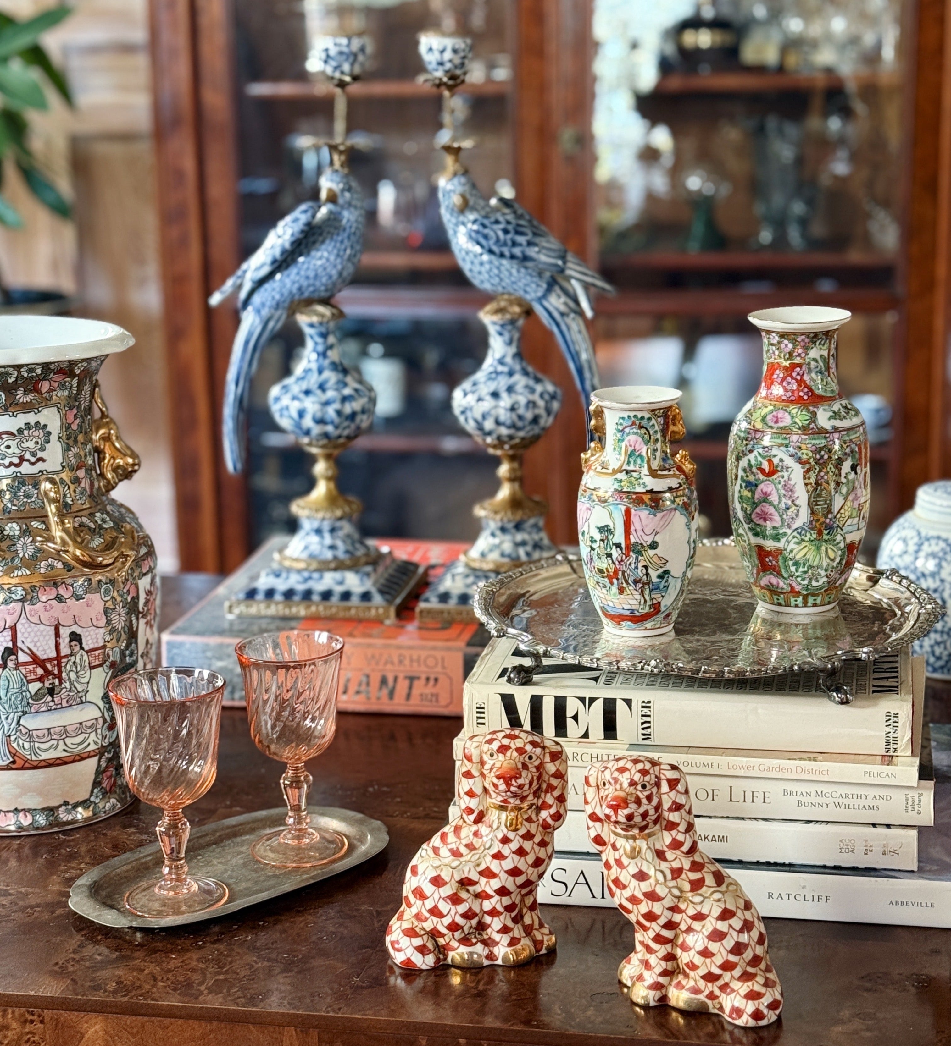 Decorative burl wood table set with vintage rose famille vases, staffordshire dogs figurines, and vintage serving trays in a room with antique furniture.