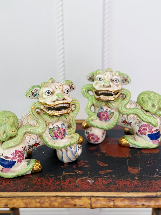 Pair of Tobacco Leaf porcelain foo dogs with green detailing and colorful floral decoration displayed on an antique chest.
