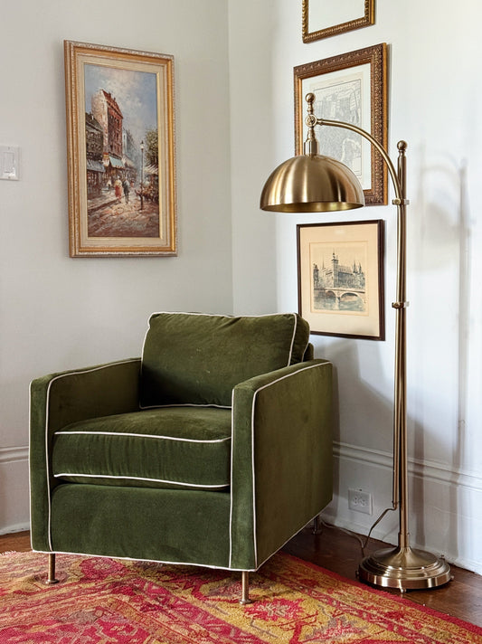 brass floor lamp with a green velvet designer chair with vintage art hanging on the walls