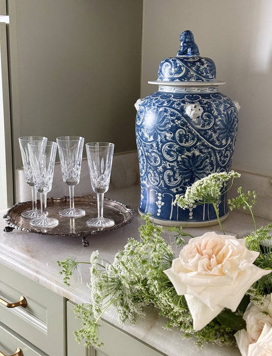 Vintage silver serving tray with crystal champagne flutes, styled alongside a blue and white porcelain ginger jar and garden roses on a marble countertop.