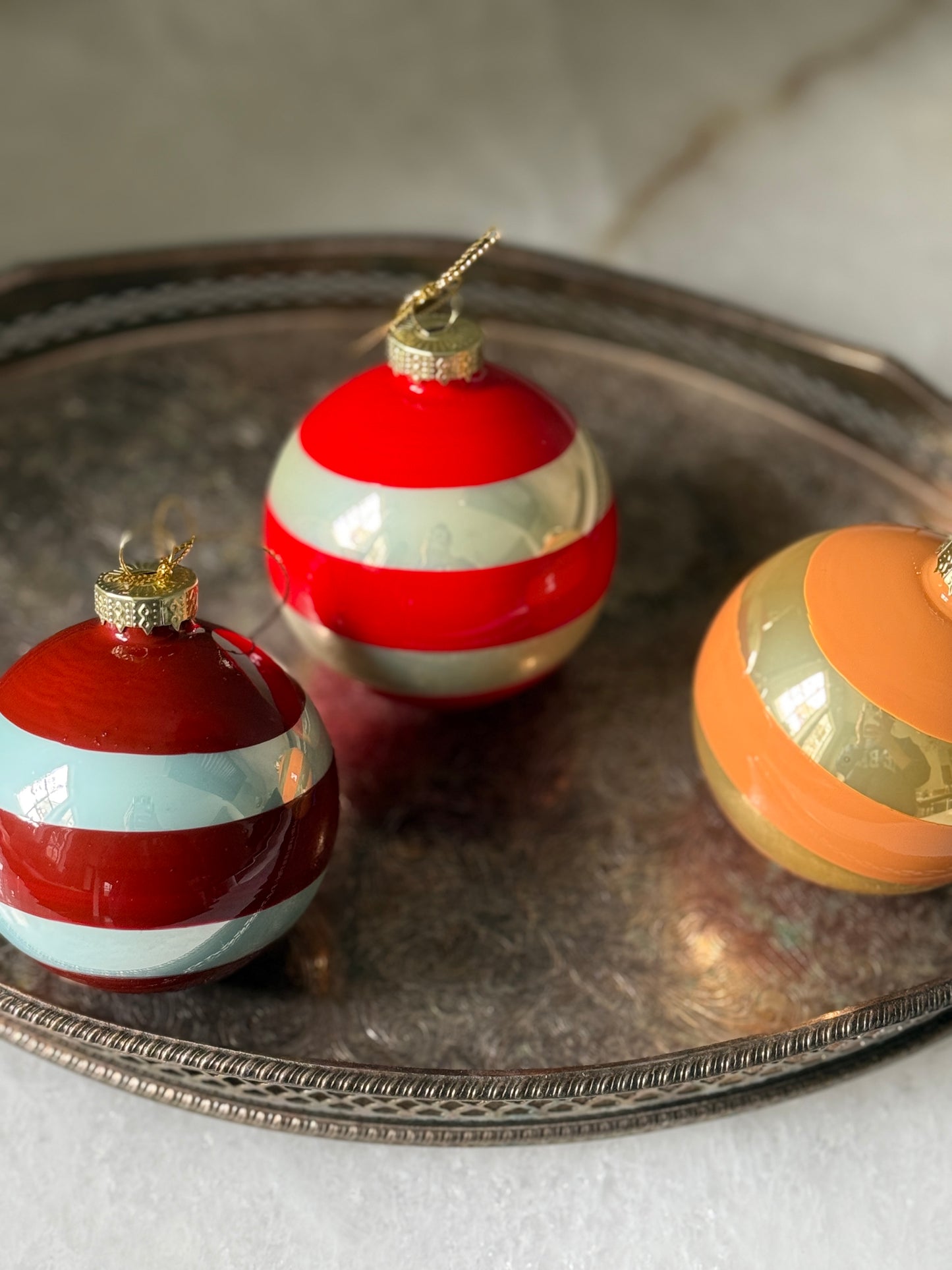 Three striped Christmas ornaments on a metallic tray with a white background