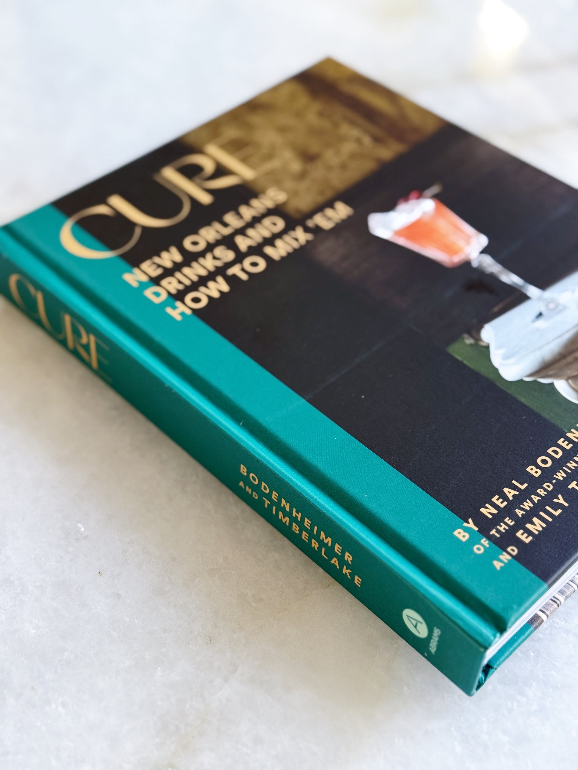 Book titled 'Cure: New Orleans Drinks and How to Mix Them' on a light background