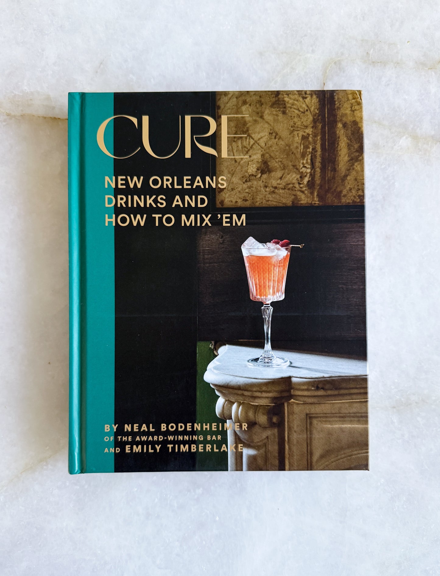 Book titled 'Cure: New Orleans Drinks and How to Mix 'Em' on a white surface