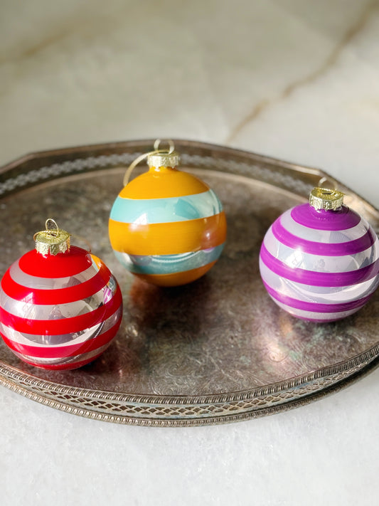 Three striped Christmas ornaments on a metallic tray with a neutral background