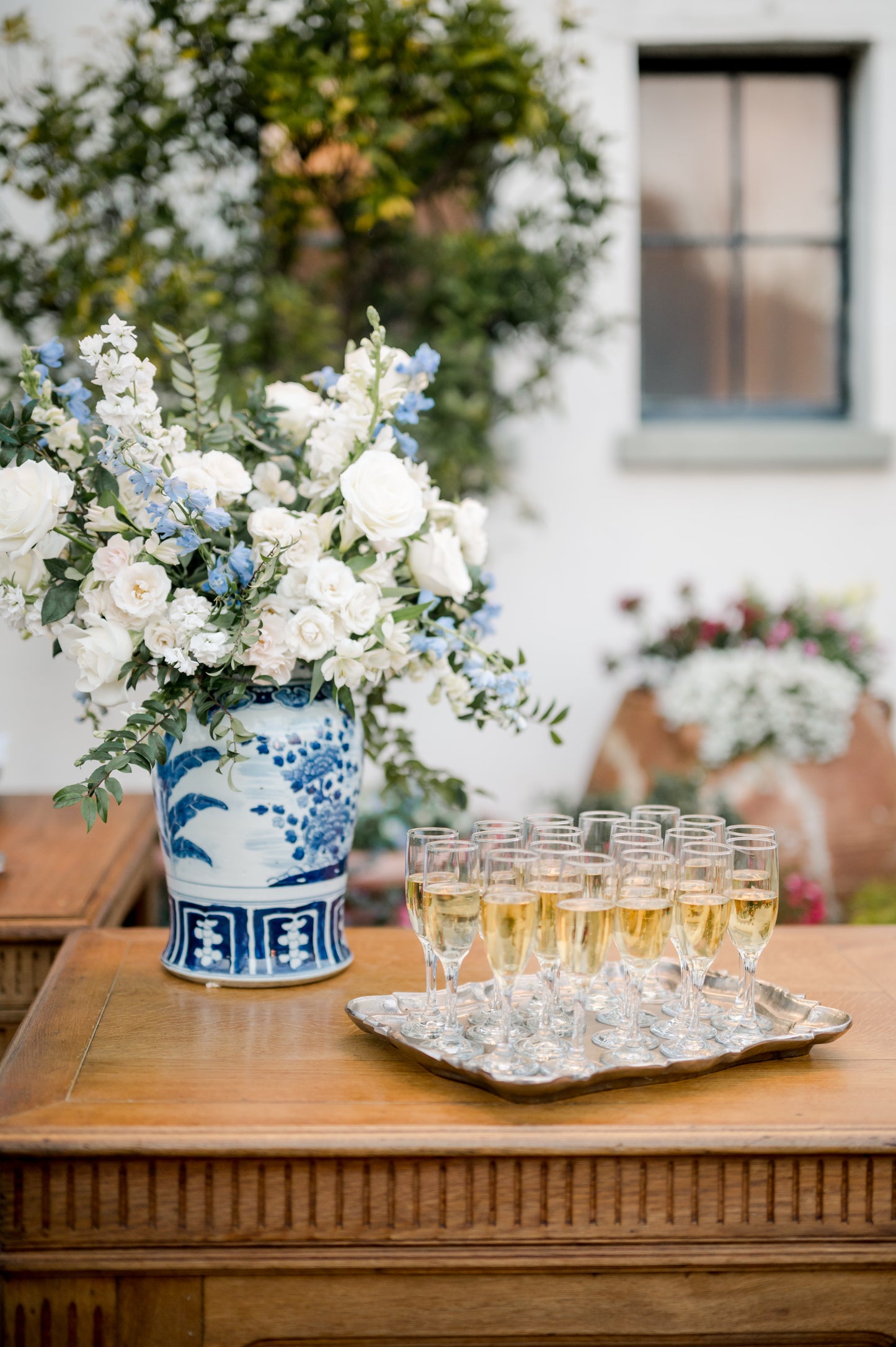 blue and white large ginger jar with foo dog lid filled with flowers next to champagne glasses