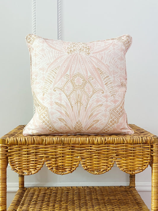 custom pillow in Schumacher cap ferrat fabric in blush on a scalloped wicker side table 